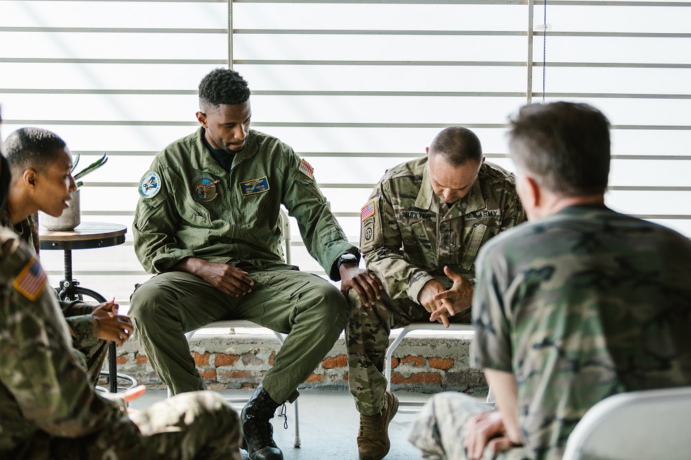 two men wearing army uniform looking distressed, army officer places his hand on army officers knee for support