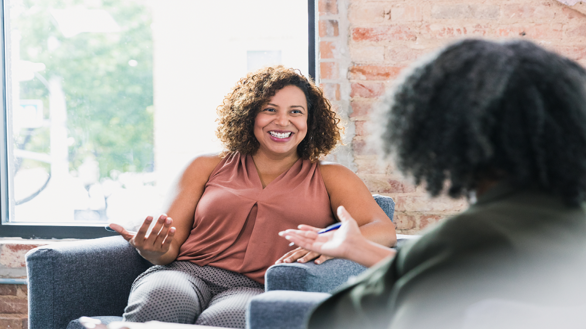 two women sitting, woman smiling widely at therapist who has hand outstretched