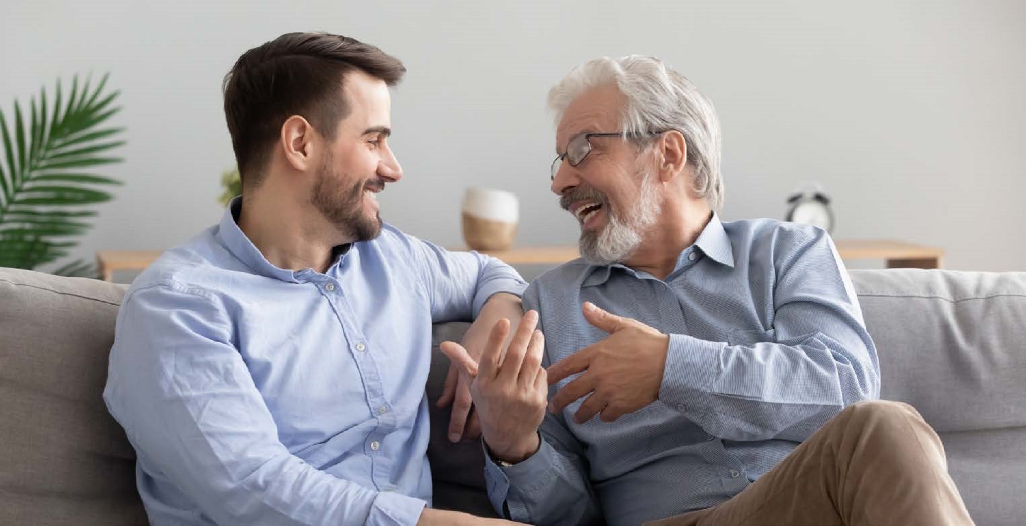 Elderly man joyfully explaining something to younger man on sofa