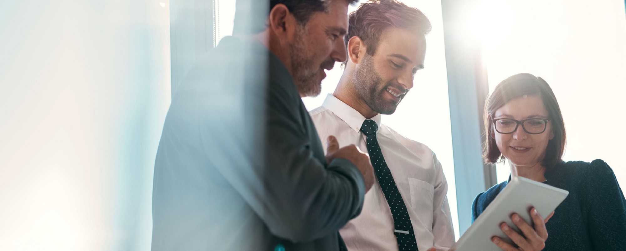 businessman smiling and showing others something on his tablet, others looking engaged