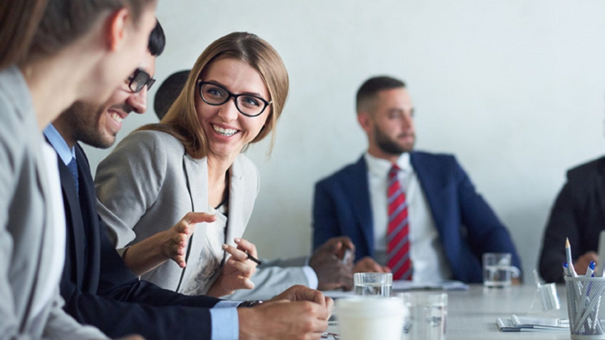 Group of business people around a desk at a meeting, main woman in focus smiling