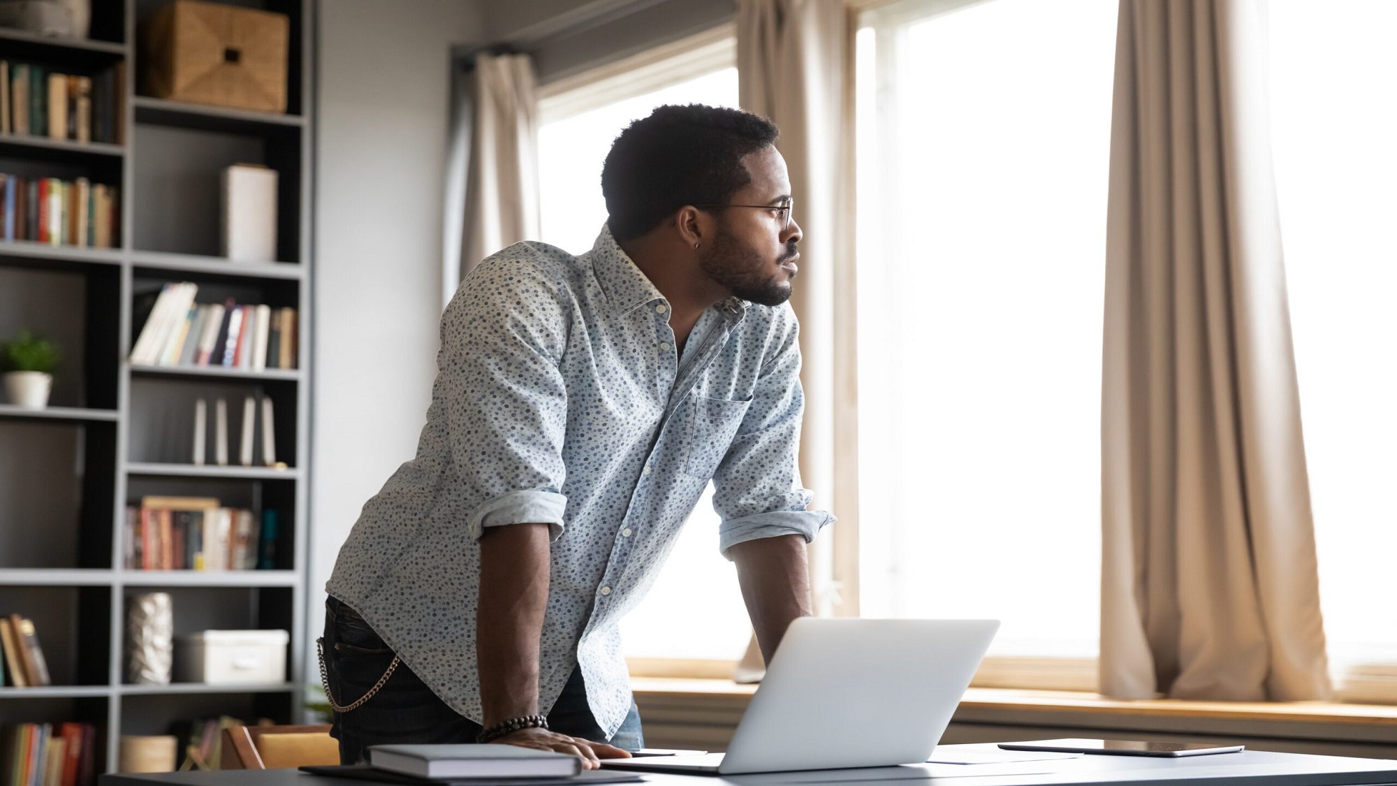 Young,Thoughtful,African,American,Businessman,Leaning,On,Table,With,Laptop,
