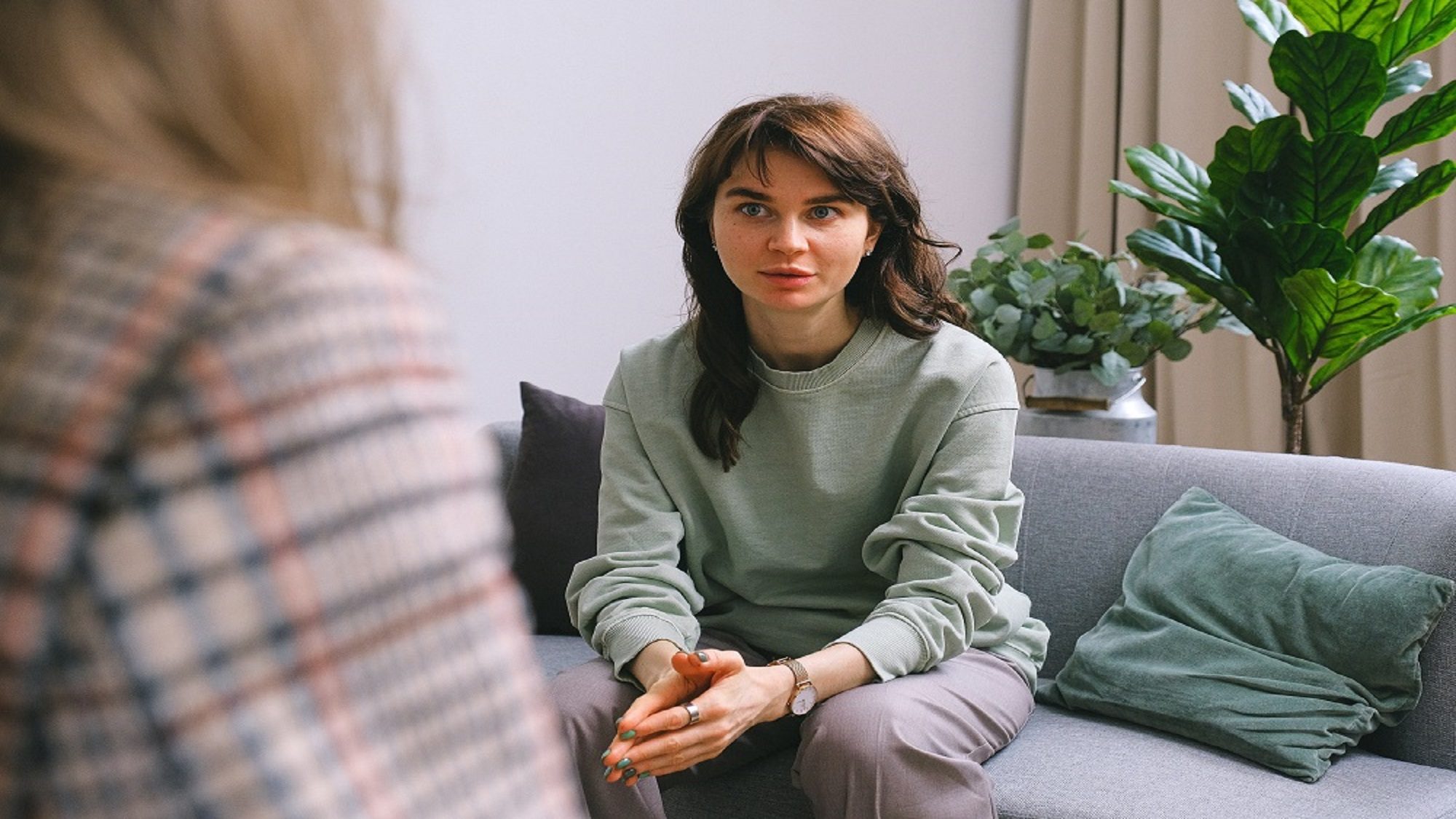 woman sitting on couch with hands clasped together talking to therapist