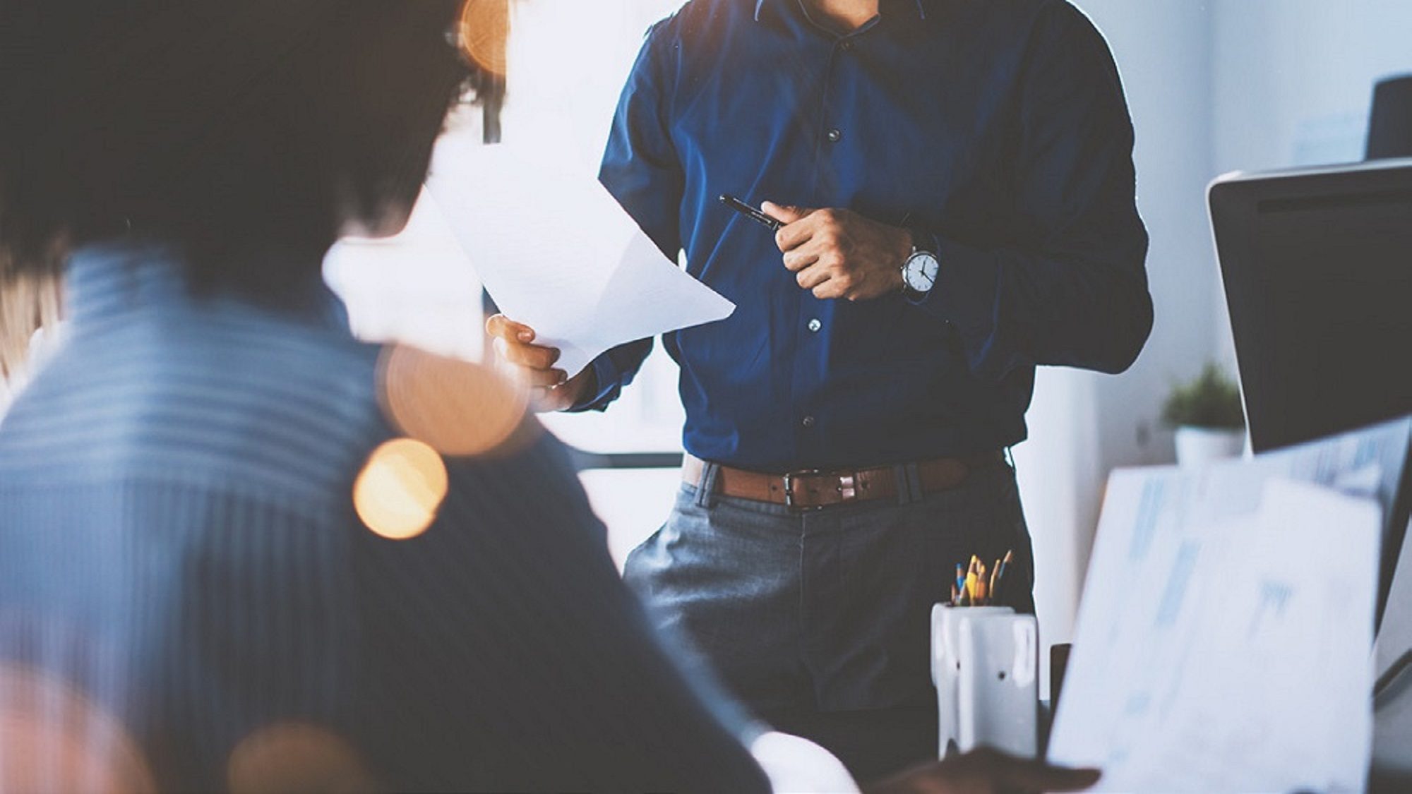 man in office holding piece of paper facing woman in suit
